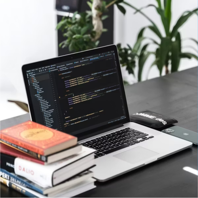 Laptop displaying code beside books and indoor plants.