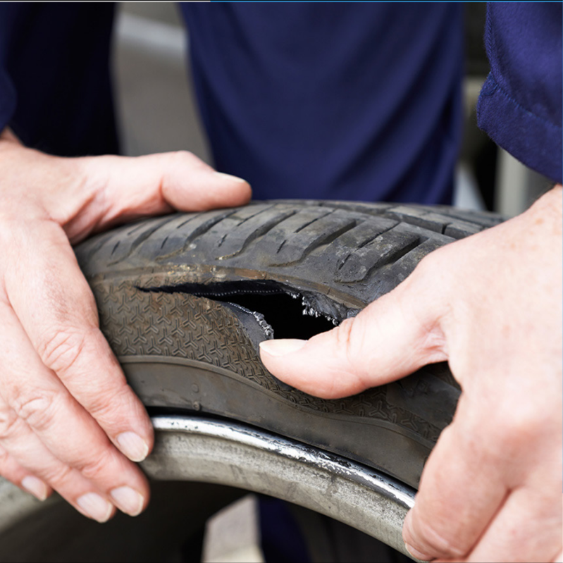 Hands inspecting damage on a vehicle tyre.