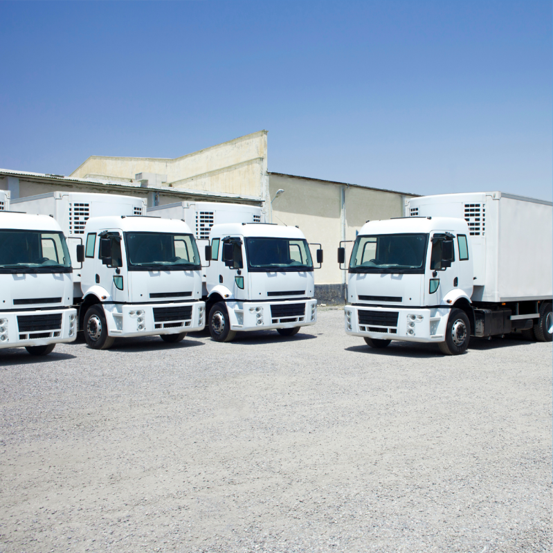 Several white commercial trucks parked outside a warehouse.