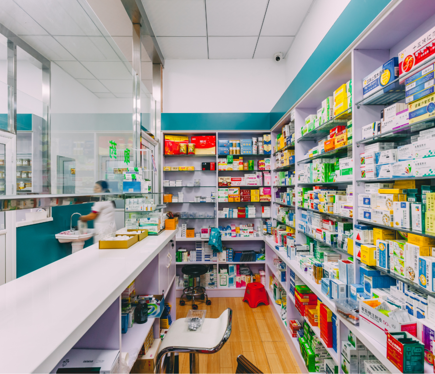 Pharmacy interior with medicine shelves, a counter, and a staff member.